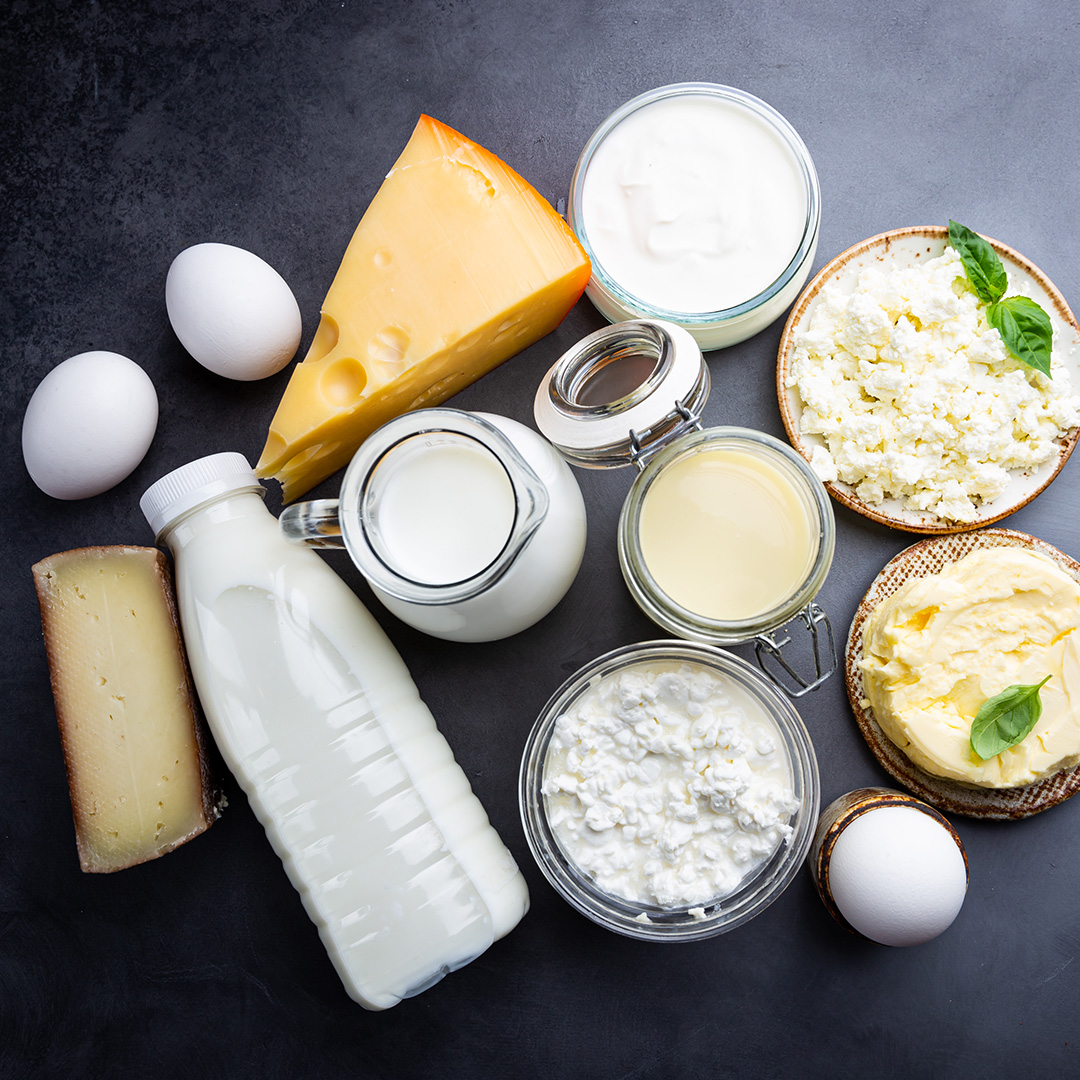 Cheese, milk, cream, butter, and eggs sit on black table