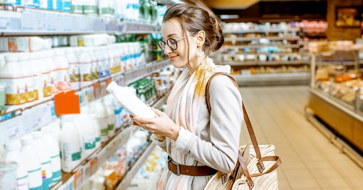 Woman with scarf and bag reads milk label in grocery store