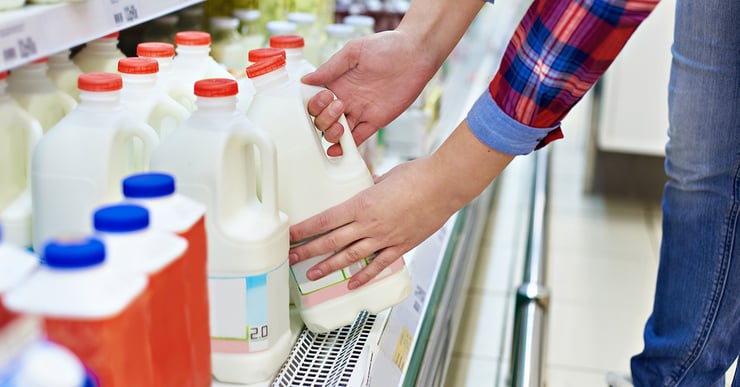 Hands pick up milk out of retail store cooler