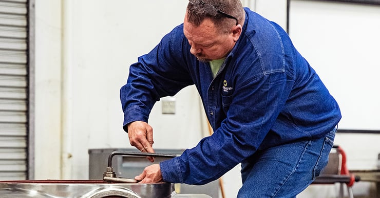 Separators employee bends down to work on industrial centrifuge frame.